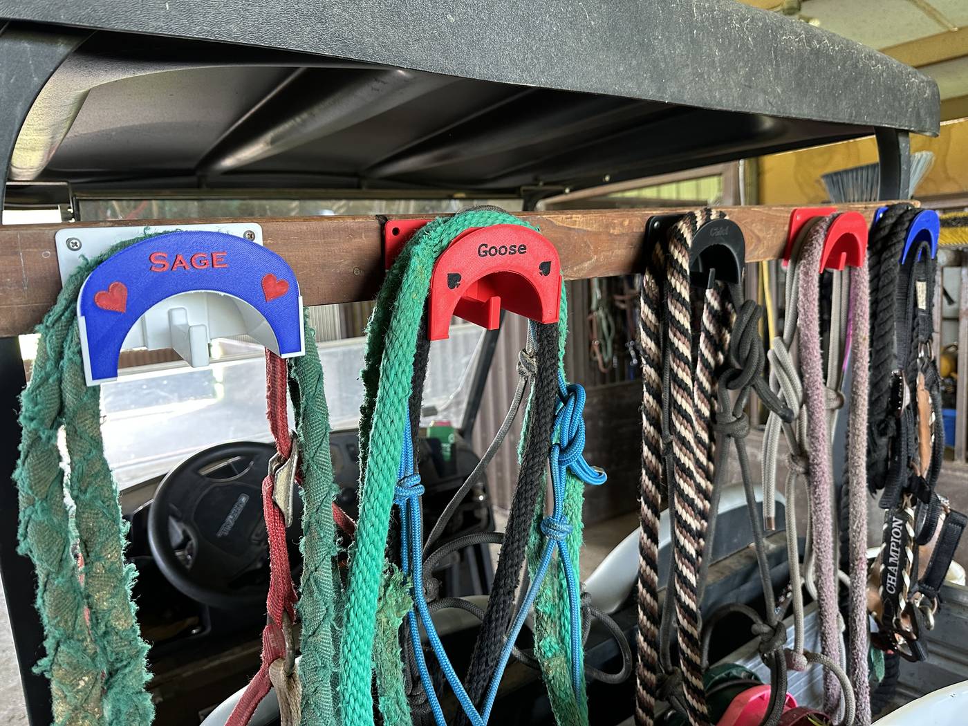 Multiple 3D-printed halter holders on golf cart rail, each labeled with a horse name